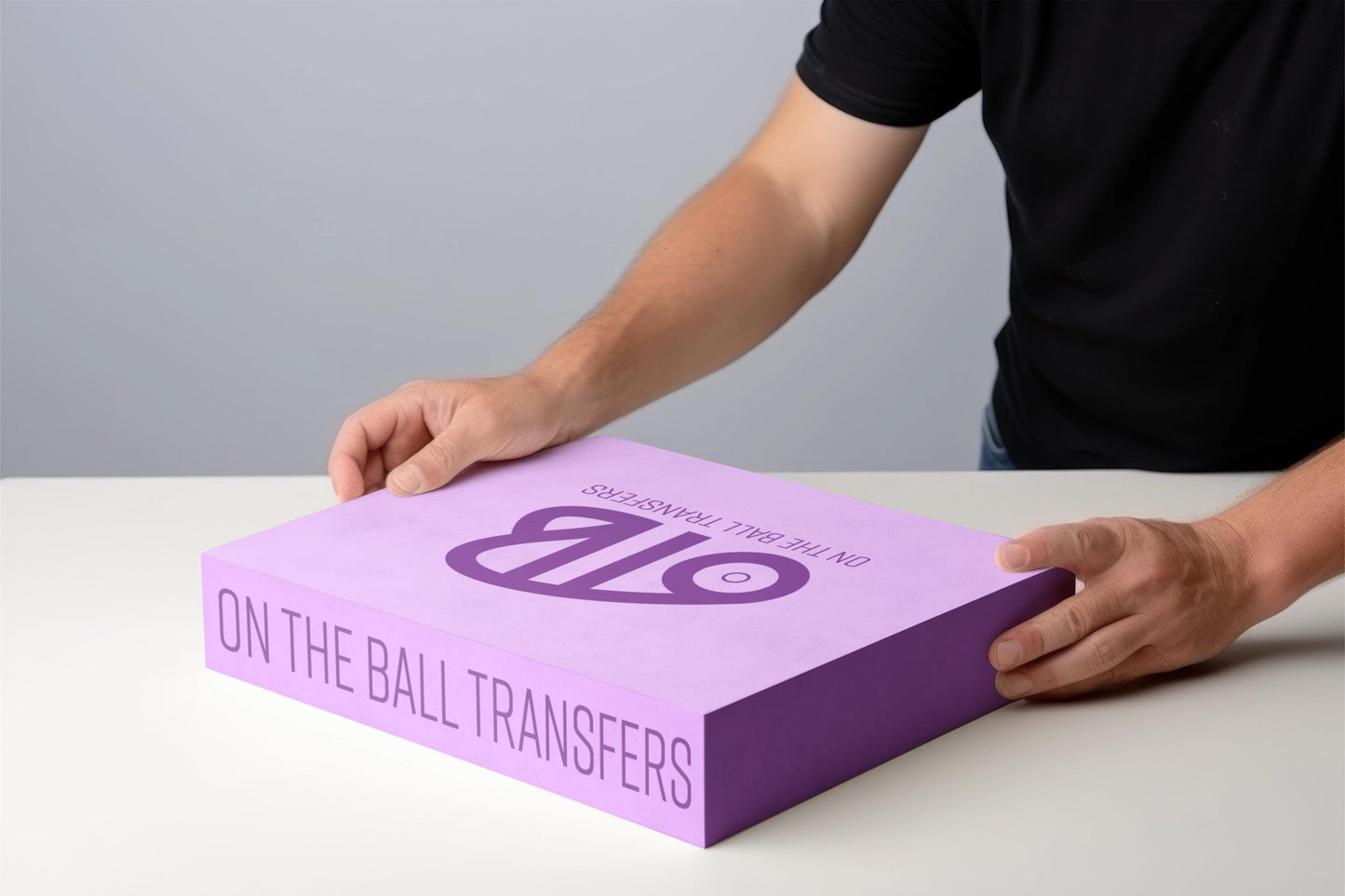 Person holding a purple box filled with dtf transfers with 'OTB' 'On the Ball transfers' branding on a gray background