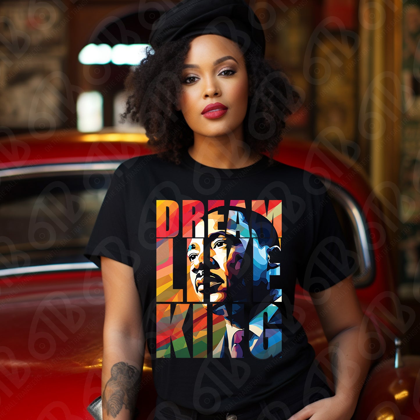 Woman wearing a black t-shirt with a colorful graphic design in front of a red car.