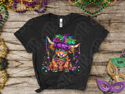 Black t-shirt with a colorful cow wearing a Mardi Gras mask on a wooden surface with Mardi Gras beads and masks.