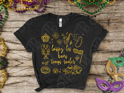 Black t-shirt with gold graphics and text on a wooden surface with Mardi Gras decorations.