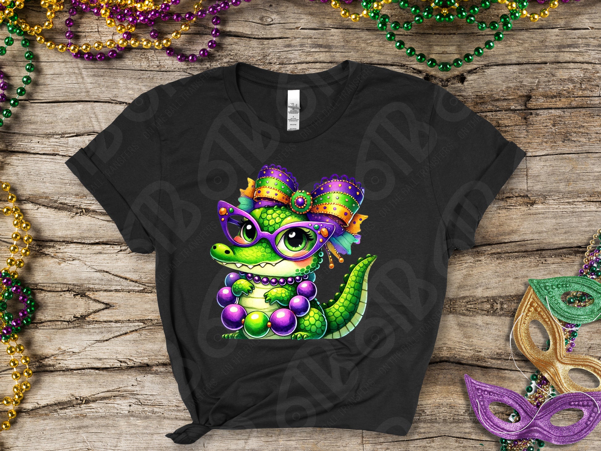 Black t-shirt with a colorful alligator design on a wooden surface with Mardi Gras beads and masks.
