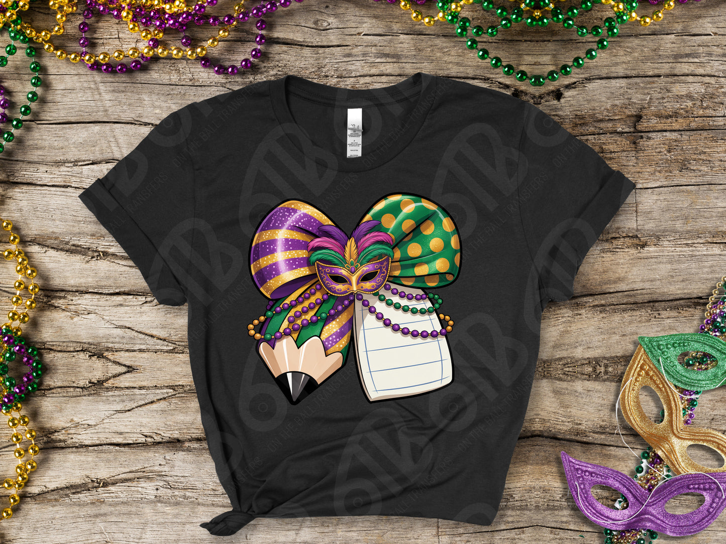 Black t-shirt with Mardi Gras-themed design on a wooden surface with festive beads and masks.