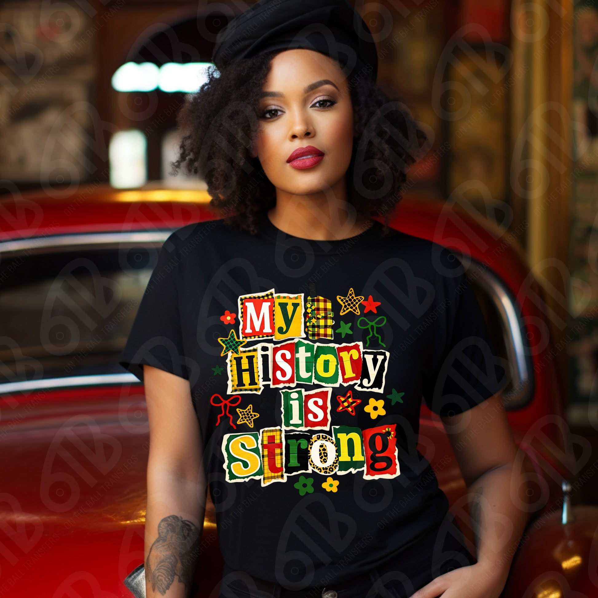 Woman wearing a black t-shirt with 'My History is Strong' text in colorful letters, sitting in a car.